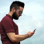 Un joven con su celular en la mano con un fondo de cielo azul y viendo su nivel de Data crédito desde su teléfono.