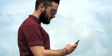 Un joven con su celular en la mano con un fondo de cielo azul y viendo su nivel de Data crédito desde su teléfono.
