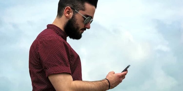 Un joven con su celular en la mano con un fondo de cielo azul y viendo su nivel de Data crédito desde su teléfono.