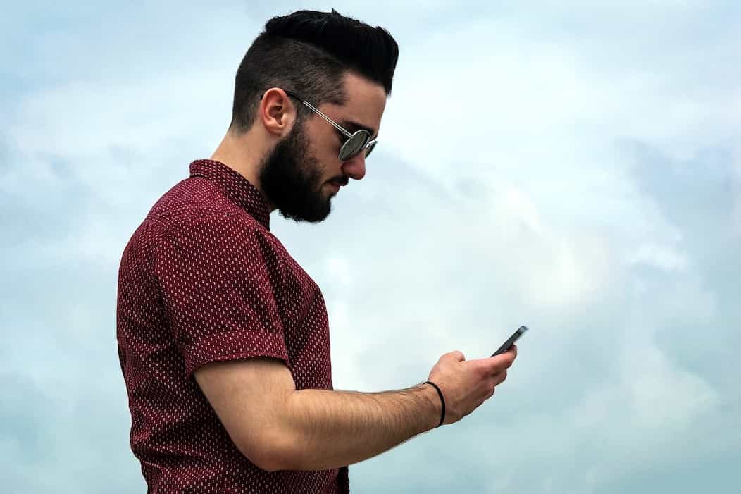 Un joven con su celular en la mano con un fondo de cielo azul y viendo su nivel de Data crédito desde su teléfono.