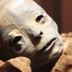 Pieza cultural arqueológica acostada con un rostro de calavera en oro.