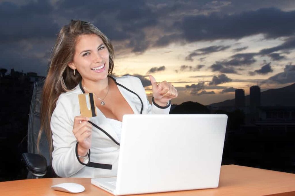 una mujer sonriendo y sosteniendo en su mano una tarjeta de crédito y haciendo compras por internet con éxito.