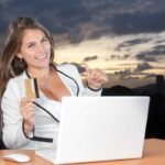 una mujer sonriendo y sosteniendo en su mano una tarjeta de crédito y haciendo compras por internet con éxito.