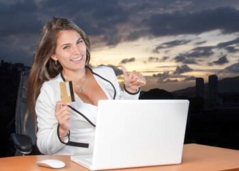 una mujer sonriendo y sosteniendo en su mano una tarjeta de crédito y haciendo compras por internet con éxito.