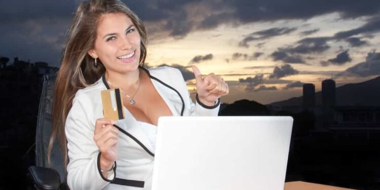 una mujer sonriendo y sosteniendo en su mano una tarjeta de crédito y haciendo compras por internet con éxito.