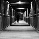 Un señor caminando con su perro en un puente oscuro de transmilenio.