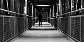 Un señor caminando con su perro en un puente oscuro de transmilenio.