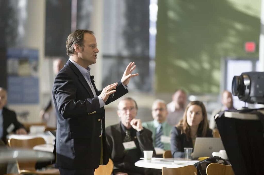 Un señor esta hablando delante de las personas, dictando una conferencia, desarrollando un evento de emprendedores y periodistas.