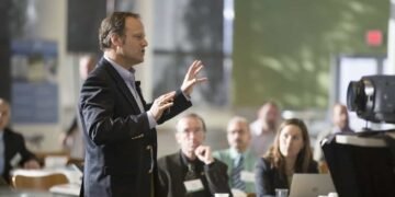 Un señor esta hablando delante de las personas, dictando una conferencia, desarrollando un evento de emprendedores y periodistas.