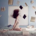 Una mujer esta sentada encima de su cama con su cabello alborotado y un montón de libros al aire, aprovecha la feria del libro en bogotá, y con ella la gran pregunta para qué ir a la feria y visitarla