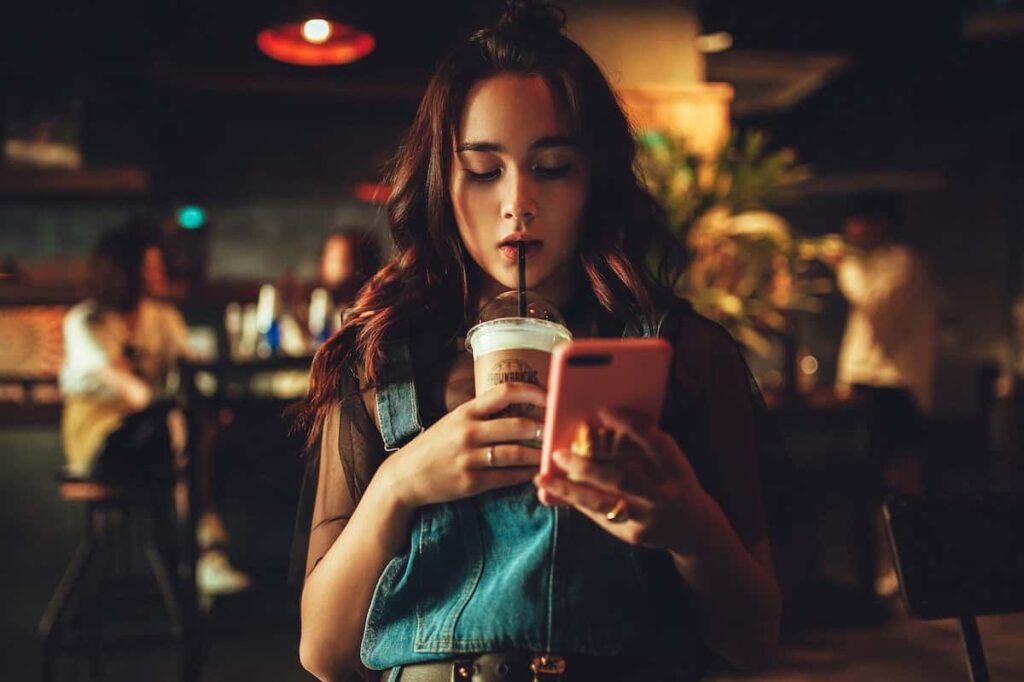 Chica en una tienda, mirando su celular y tomando cafe.