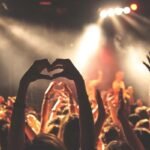 Personas con los brazos arriba haciendo un corazón en medio de un concierto.