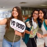 Mujeres jóvenes están participando en política con unas banderas en las manos que dice yo voto.