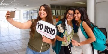 Mujeres jóvenes están participando en política con unas banderas en las manos que dice yo voto.