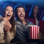 Una pareja esta en el cine sorprendida viendo el Guason y comiendo palomitas de maís.