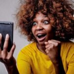 Una mujer mirando su celular sonriendo de alegría