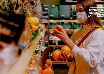 Una mujer con tapabocas haciendo mercado y agarrando una fruta.