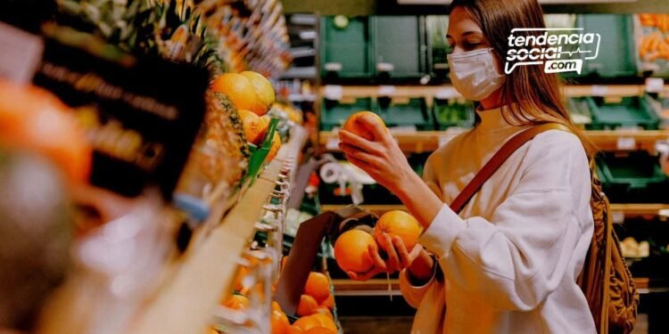 Una mujer con tapabocas haciendo mercado y agarrando una fruta.