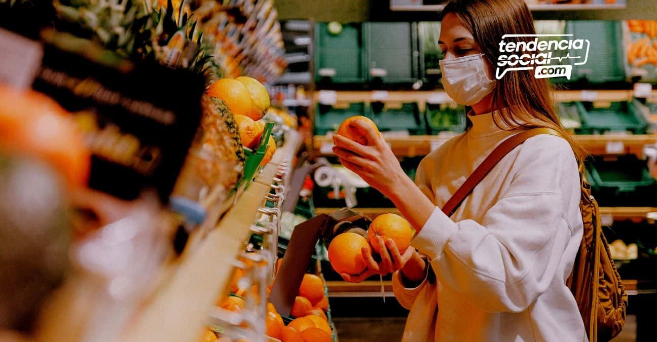 Una mujer con tapabocas haciendo mercado y agarrando una fruta.