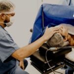 Un médico esta sentado atendiendo a un paciente acostado y tocándole la cabeza