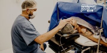 Un médico esta sentado atendiendo a un paciente acostado y tocándole la cabeza