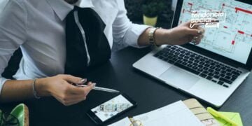 Una persona esta sentada en su escritorio usando un computador y celular