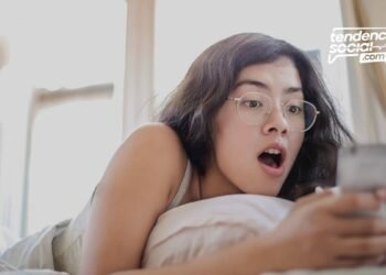 Mujer acostada en la cama sorprendida mirando su celular