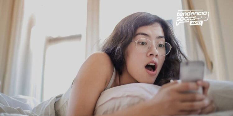 Mujer acostada en la cama sorprendida mirando su celular