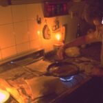 Una mujer en la cocina sin luz con una vela corte de luz en soacha por mantenimiento