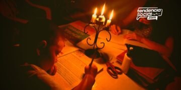 Un niños haciendo tareas en la mesa en medio de unas velas sin luz en Soacha y en la casa